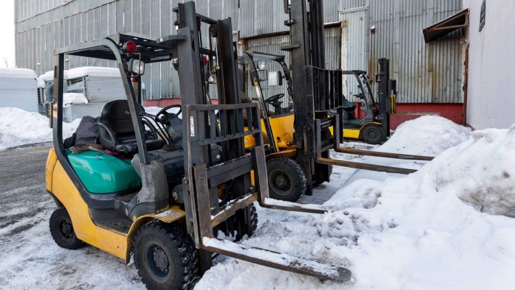 Three outdoor forklifts parked next to piles of snow
