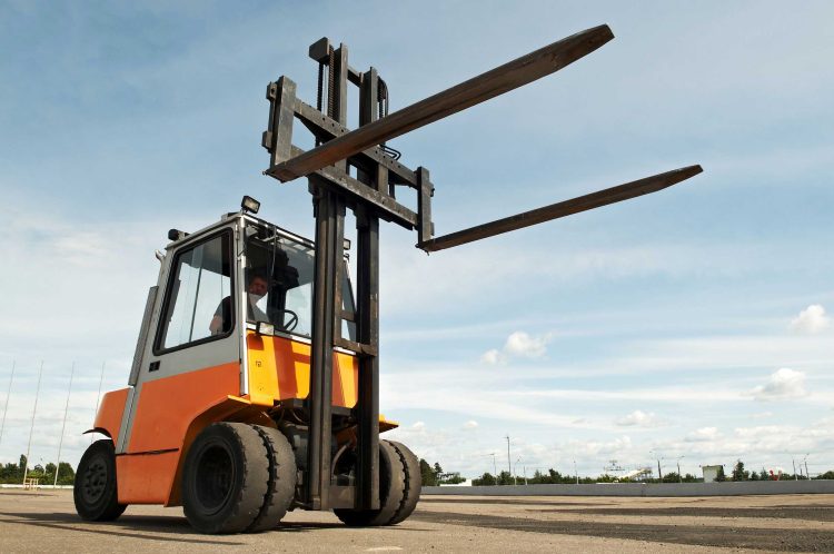 Orange off-road forklift on the pavement with lifted forks