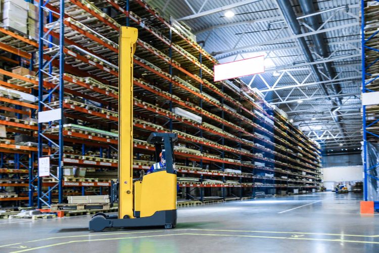 Yellow stand-up reach forklift in the middle of a warehouse aisle