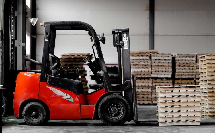 Red counterbalance truck moving stacks of pallets in a warehouse