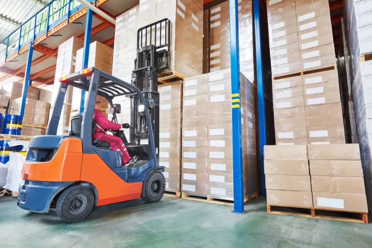Operator in red operating an orange forklift to lift a pallet of boxes