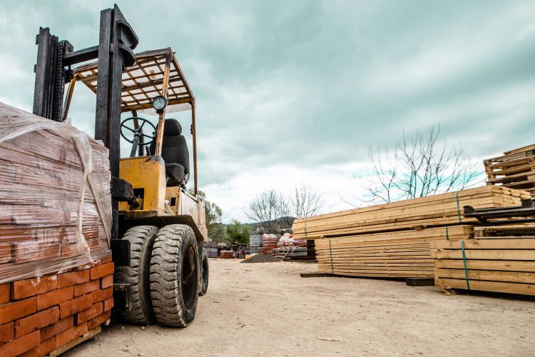 Large all-terrain forklift loaded with a pallet of bricks at a construction site