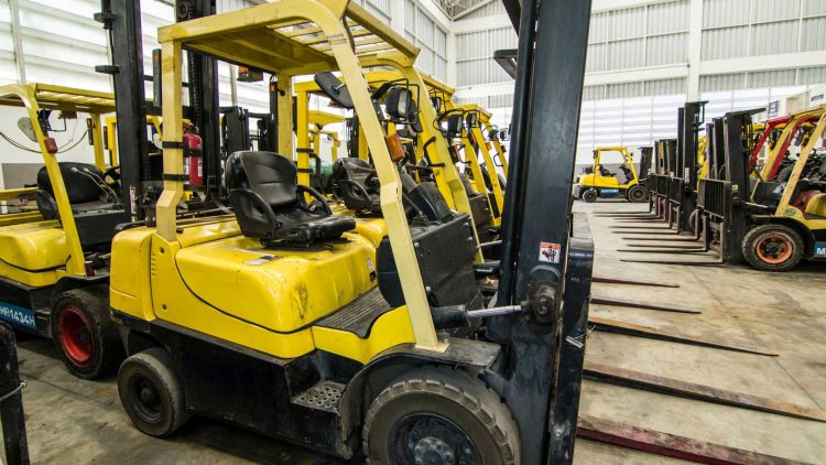 Electric forklift maintenance being performed on electric forklifts in a warehouse lot.